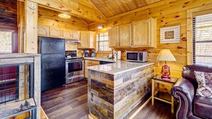 A cozy cabin-style kitchen with wooden walls, a central island, and a dining area with a leather couch. - Tennessee Chalet (Gatlinburg)