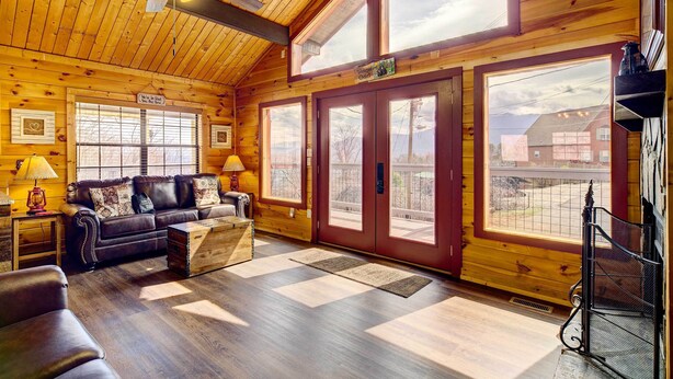 A cozy cabin interior with a wooden ceiling, a leather sofa, a wooden coffee table, and large windows offering views of the outside. - Tennessee Chalet (Gatlinburg)
