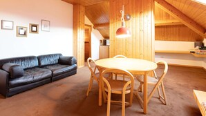A cozy room with a wooden ceiling, a black leather sofa, a wooden dining table with chairs, and framed pictures on the wall. - Castle in Clouds; A Holiday Home (Stenico)
