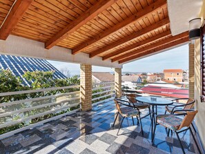 Un espace extérieur abrité, doté d’un sol à carreaux, de poutres en bois au plafond et offrant une vue sur les bâtiments situés au loin.