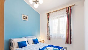 Quarto com cama, mesa de cabeceira, janela com cortinas e luminária no teto.