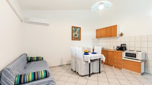 Um espaço compacto com sofá, mesa de jantar e cadeiras, cozinha com armários e eletrodomésticos, e luminária no teto.