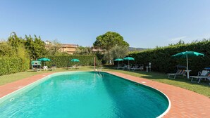 A rectangular swimming pool with a brick border, surrounded by green umbrellas and lounge chairs.