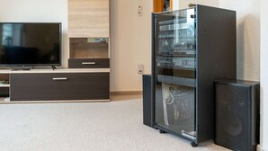Moderni olohuone, jossa on litteänäyttöinen televisio, puinen kaappi, lasiovilla varustettu viihdekeskus ja musta kaiutin.