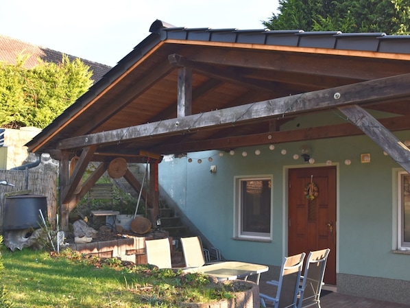 A rustic building with a sloped roof, a wooden staircase, and a patio area with outdoor furniture.