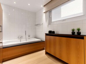 Une salle de bain moderne avec une baignoire sur pieds, un meuble-lavabo en bois et une fenêtre laissant entrer la lumière naturelle.