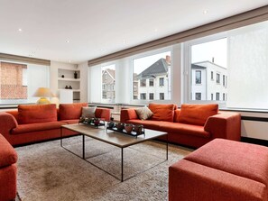 Ein modernes Wohnzimmer mit einer roten Sofagarnitur, einem Couchtisch und großen Fenstern mit Blick auf Gebäude.