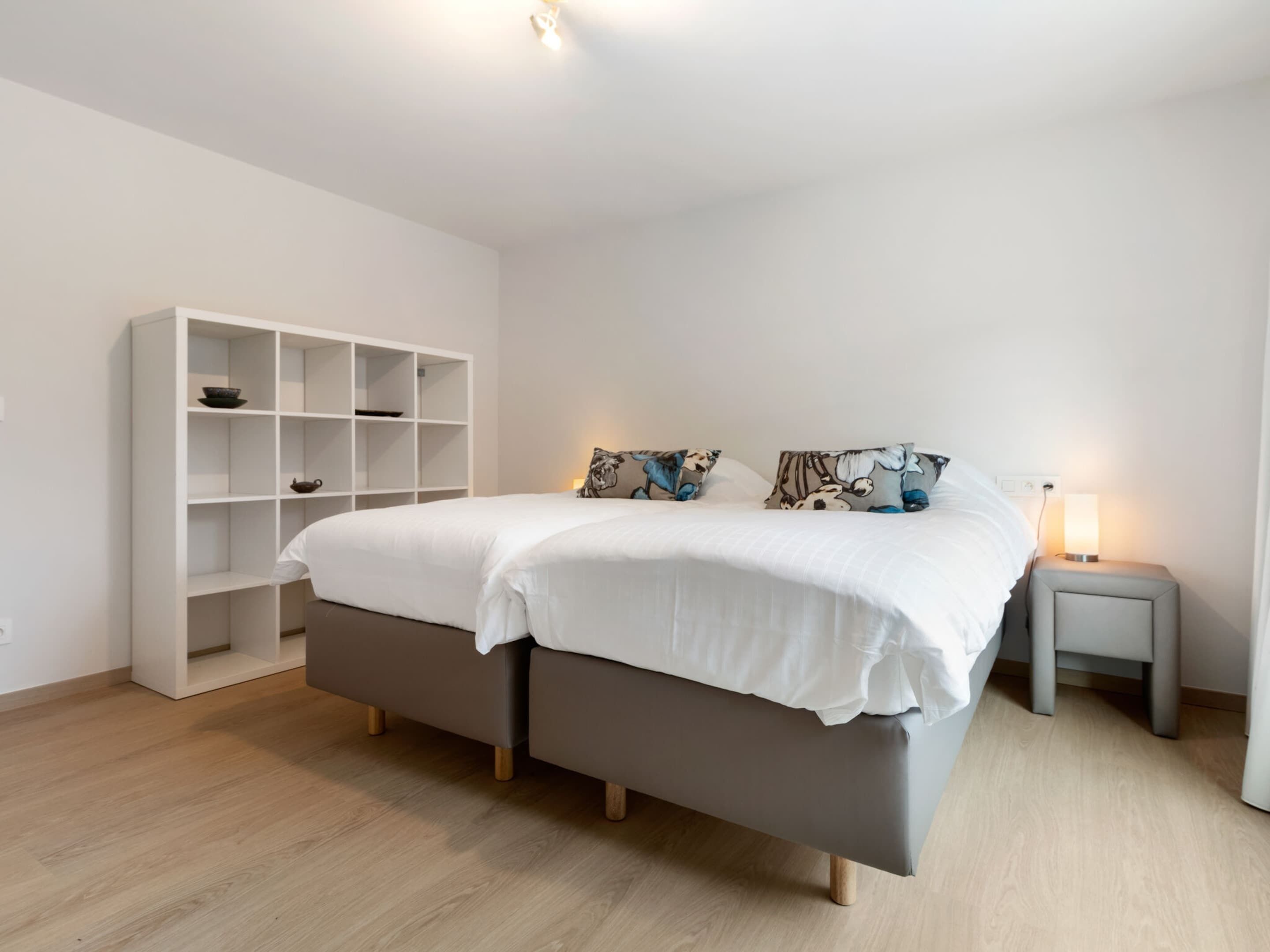 A bedroom with a bed, a white shelving unit, and a bedside table with a lamp.