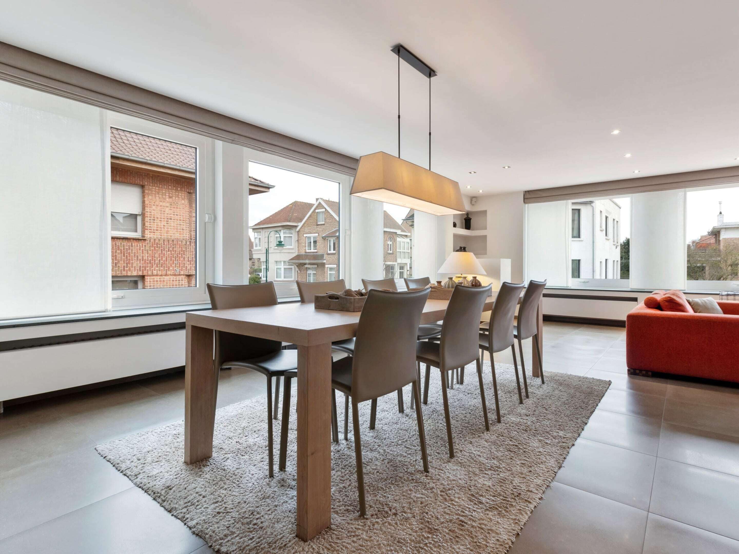 A modern dining area with a wooden table and chairs, a rug, and a red sofa.