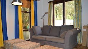 Uma sala de estar com um sofá cinza, pufes de vime e um abajur.