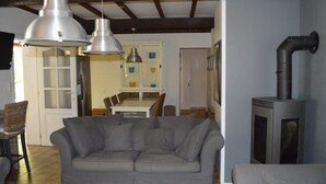 Uma sala de estar com um sofá cinza, duas luminárias pendentes, uma lareira e um espaço de jantar com cadeiras e uma mesa.