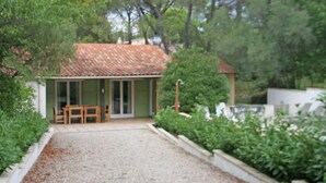 Uma pequena casa com telhado de telhas, um pátio com mesa e cadeiras, e um caminho de cascalho que leva à entrada.