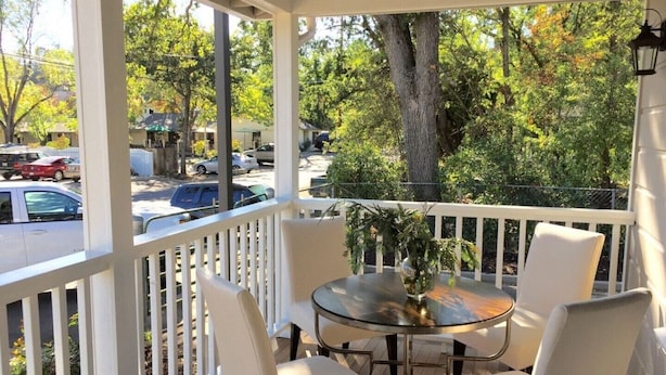 A covered outdoor seating area with a glass table and white chairs, overlooking a street with parked cars and trees. - Downtown Location, Uptown Elegance! Re-Modeled “Murphys Original School House" (Murphys)