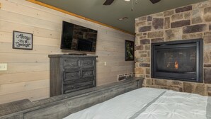 Une chambre avec un mur en pierre, une cheminée, un téléviseur fixé au-dessus de la cheminée et une commode en bois.