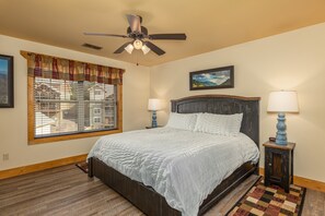 A bedroom with a bed, a ceiling fan, a window with blinds, two bedside lamps, and a painting on the wall. - Wet and Wild (Gatlinburg)