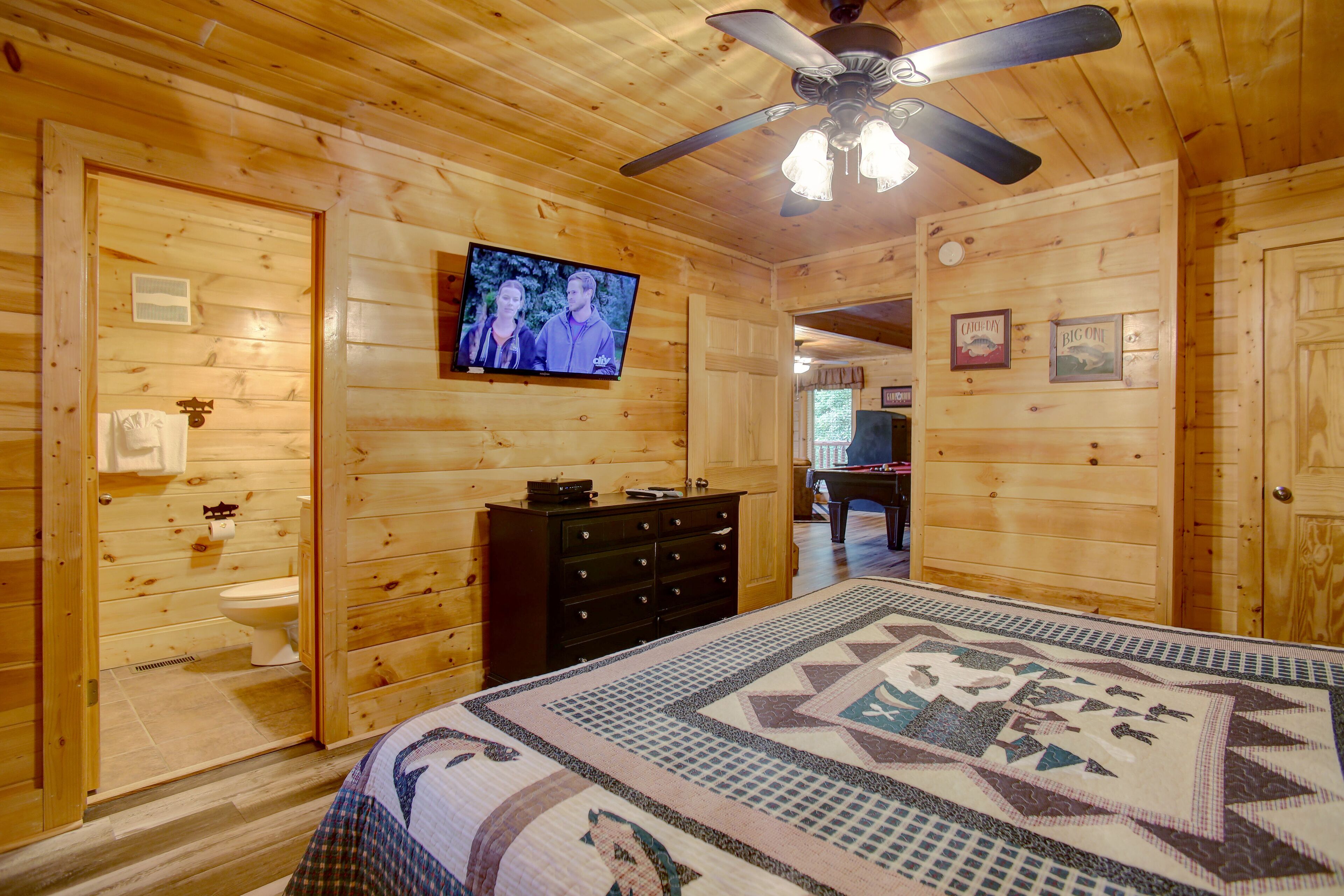 L’intérieur d’une cabane en bois, avec un lit, une commode, un téléviseur et un ventilateur de plafond.