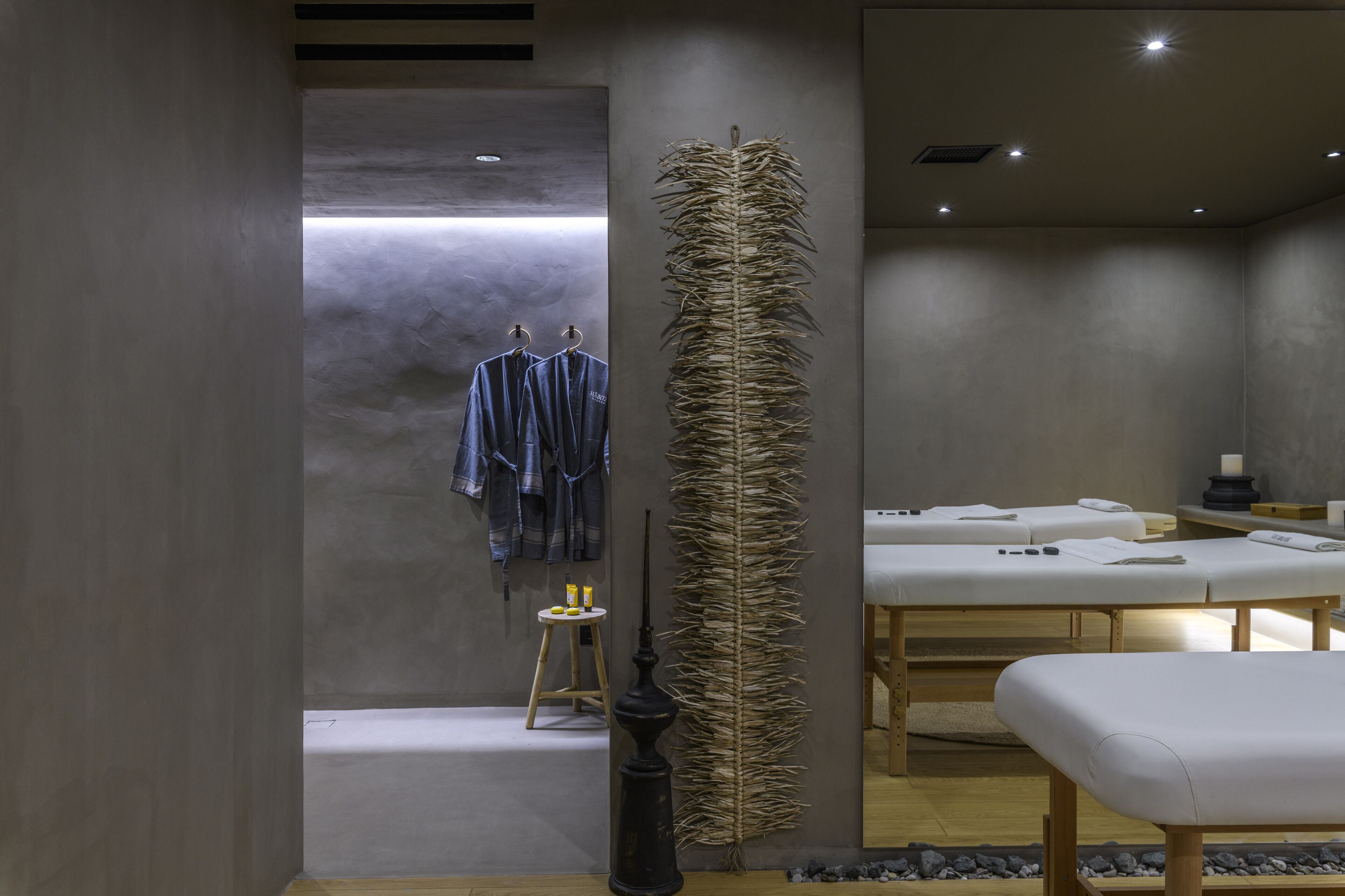 A spa room with a modern design, featuring a large wall-mounted feather sculpture, a wooden stool with bottles, and a massage table with towels.
