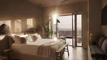 A bedroom with a large bed, a bench, a sofa, and a view of the outdoors.
