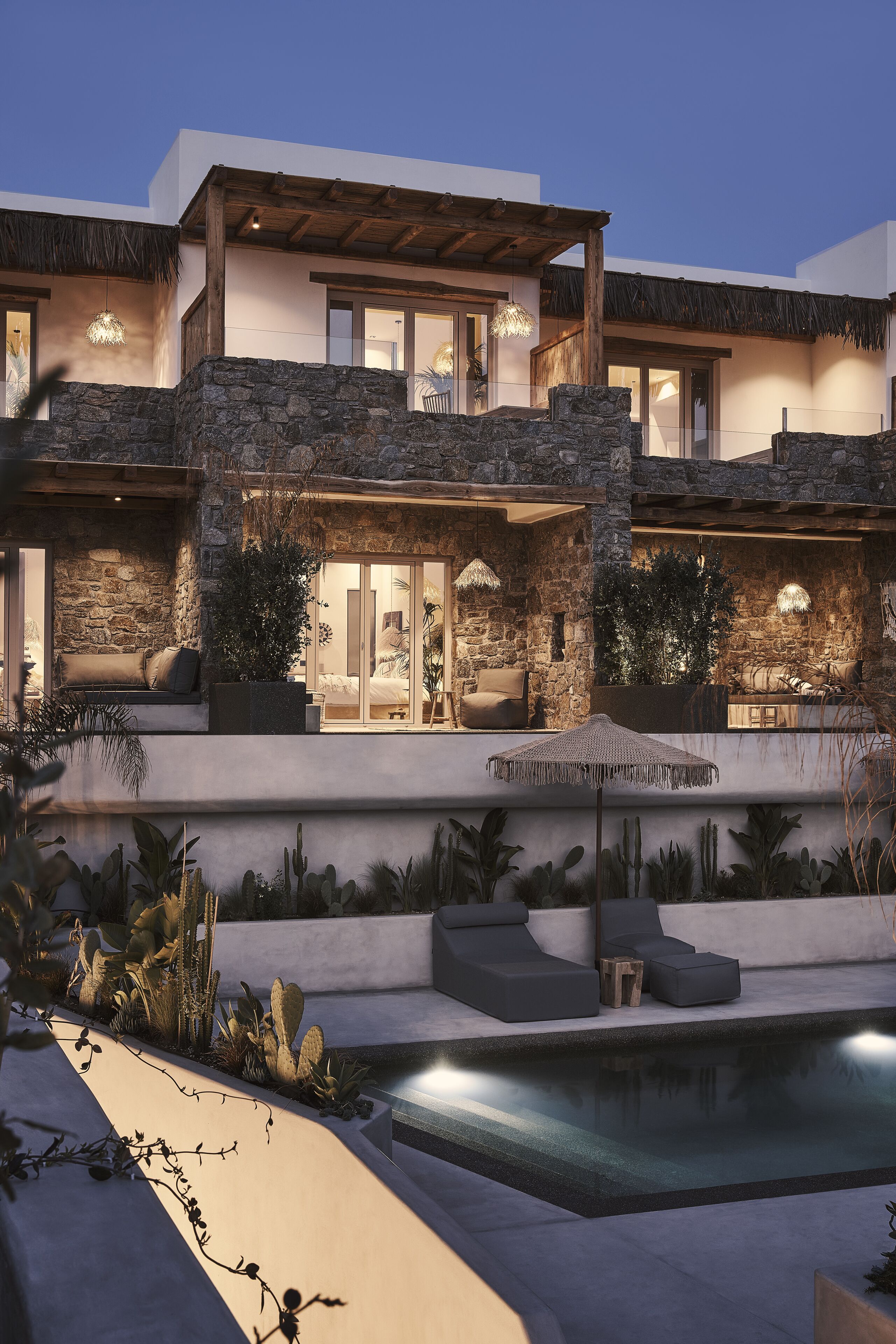 Une maison moderne avec une façade en pierre, une piscine et un espace salon extérieur.