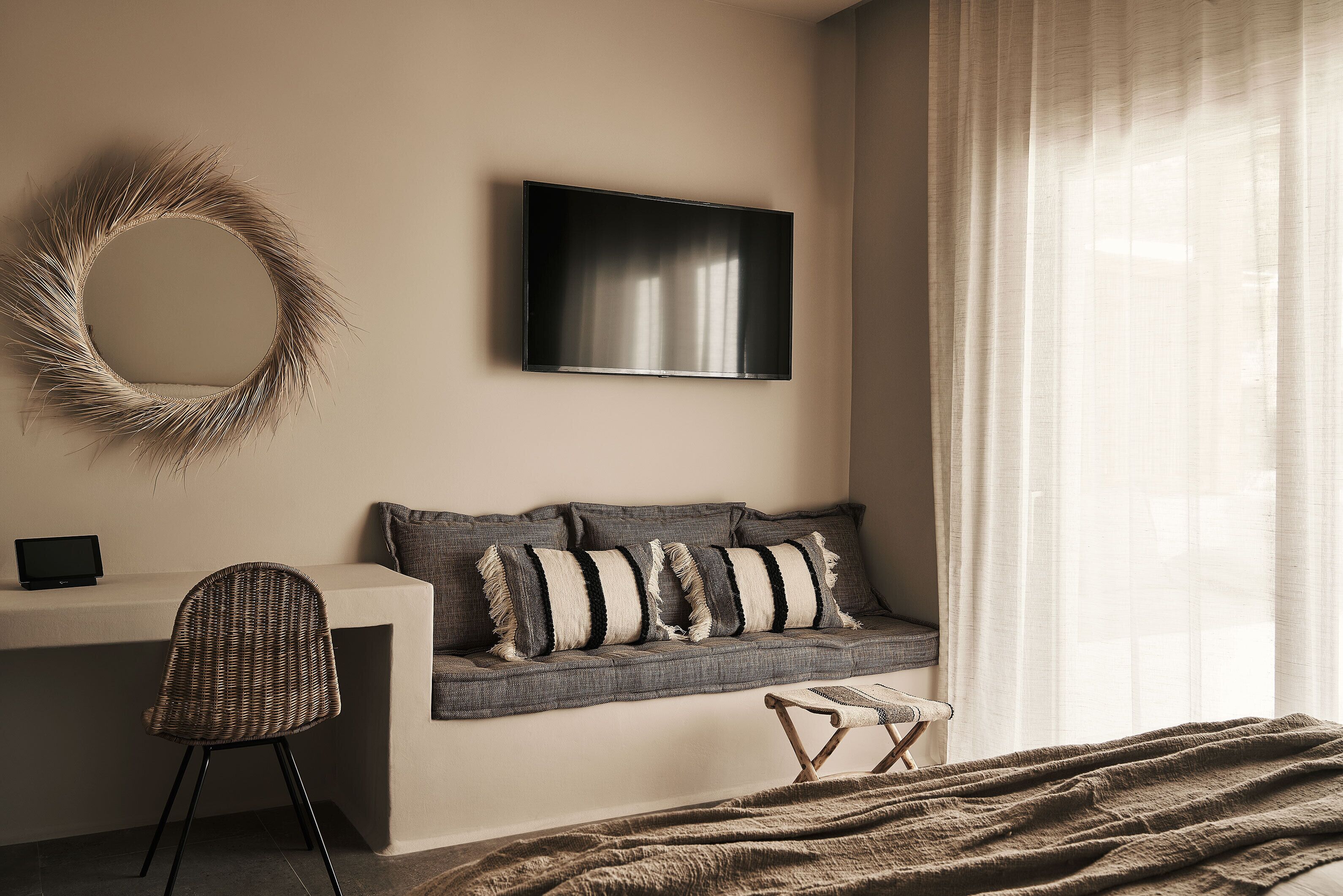 A modern bedroom with a bed, a bedside table, a chair, a sofa, a TV, and a window with curtains.