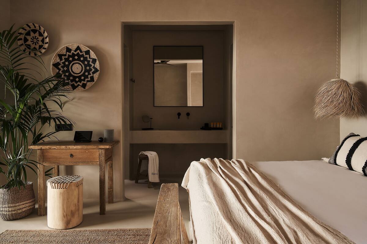 A bedroom with a bed, a wooden desk, a mirror, and a plant.