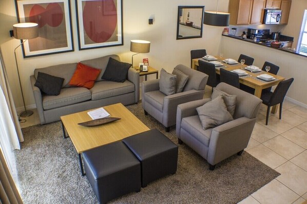 Una sala de estar moderna con un sofá, dos sillones, una mesita de centro y un comedor con una mesa dispuesta para cuatro.