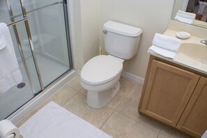 Un baño con cabina de ducha de vidrio, inodoro blanco y tocador de madera con lavamanos y espejo.