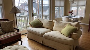 Ein Wohnzimmer mit einem beigen Sofa, einem gestreiften Sessel und einem Ottomanen mit Knopfheftung.