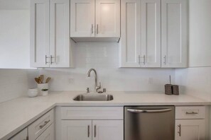 A modern kitchen with white cabinets, a stainless steel sink, and a dishwasher. - The Buccaneer House - Oceanfront (Oceanside)