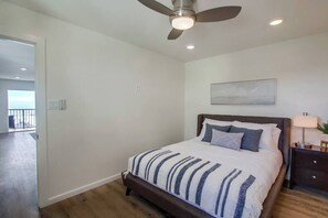 A bedroom with a bed, a ceiling fan, a nightstand, and a painting on the wall.