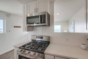 A modern kitchen with stainless steel appliances, white cabinetry, and a large window providing natural light. - The Buccaneer House - Oceanfront (Oceanside)