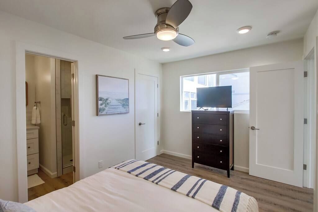 Ein Schlafzimmer mit Bett, Kommode, Fernseher auf einem Schrank, Deckenventilator und Fenster.