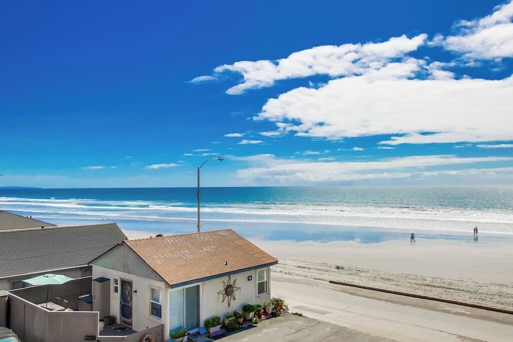 A beachfront property with a small house, a visible garage, and a clear view of the ocean.