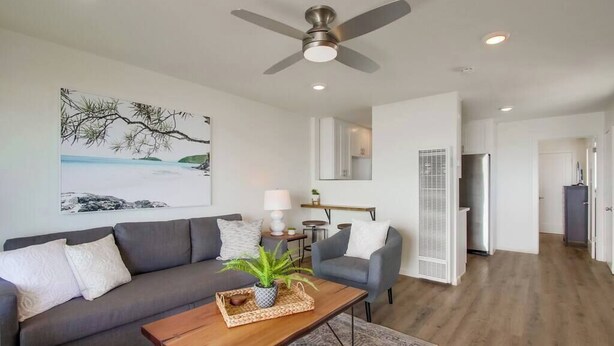 A modern living room with a grey sofa, a wooden coffee table, and a ceiling fan. - The Buccaneer House - Oceanfront (Oceanside)