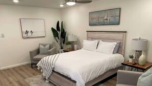 A bedroom with a bed, a chair, a nightstand, a lamp, and a painting on the wall.