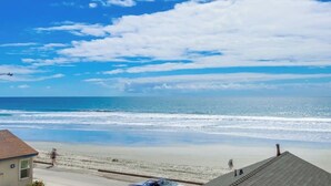 A beach view with a clear sky, a sandy shore, and a few people walking.