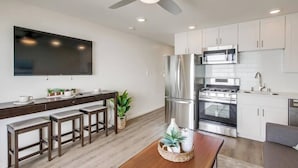 A modern kitchen with a flat-screen TV, stainless steel appliances, and a dining area with stools.