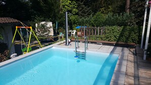 A swimming pool with a wooden deck, a swing set, and a wooden fence. - '4er Müggelwaldzimmer' quiet + cozy apartment in Köpenick m. Garden area (Bezirk Treptow-Köpenick)