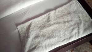 Cama com lençol branco e toalha cinza.