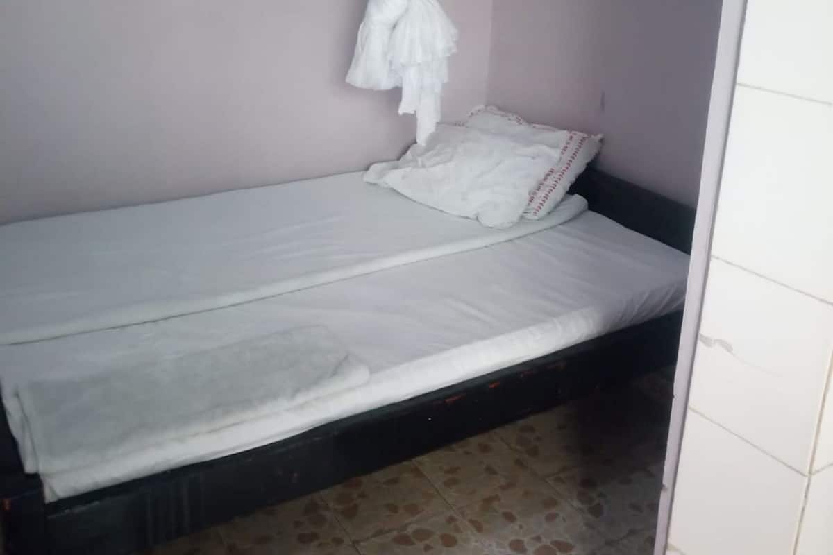 A single bed with a white mattress and pillows, a mosquito net hanging above, and a tiled floor.