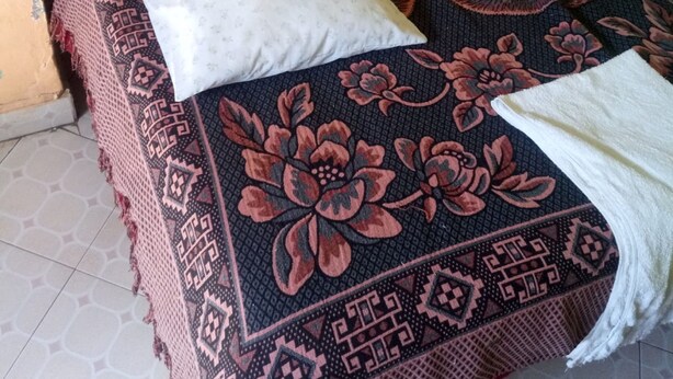 A bed with a patterned bedspread, a white pillow, and a white towel. - Eldama Lodge (Gilgil)