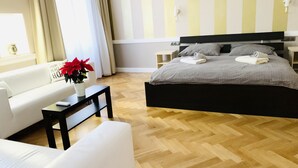 Een moderne slaapkamer met een groot bed, een witte bank, een klein tafeltje en een kamerplant.