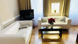Een woonkamer met een witte bank, een salontafel met een vaas, en een televisie op een meubel.