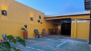 A courtyard with a yellow wall, outdoor seating, and potted plants.