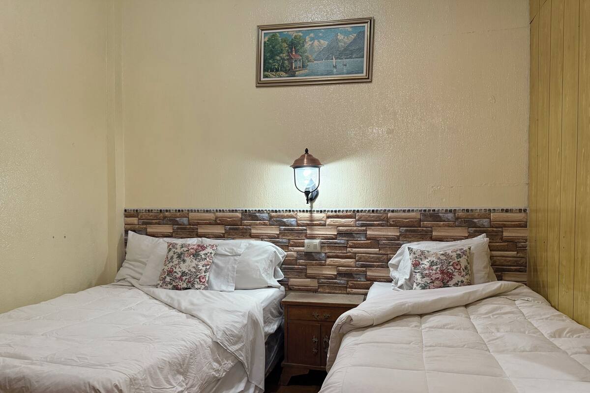 Een hotelkamer met twee bedden, een houten hoofdbord, een schilderij aan de muur en een wandlamp.