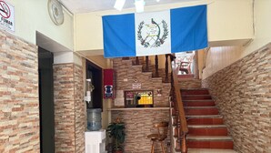 A hotel lobby with a staircase, a water dispenser, a sign indicating a smoking area, and a flag.