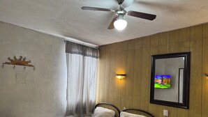 A bedroom with a bed, a ceiling fan, a wall-mounted TV, and a wooden panel wall.