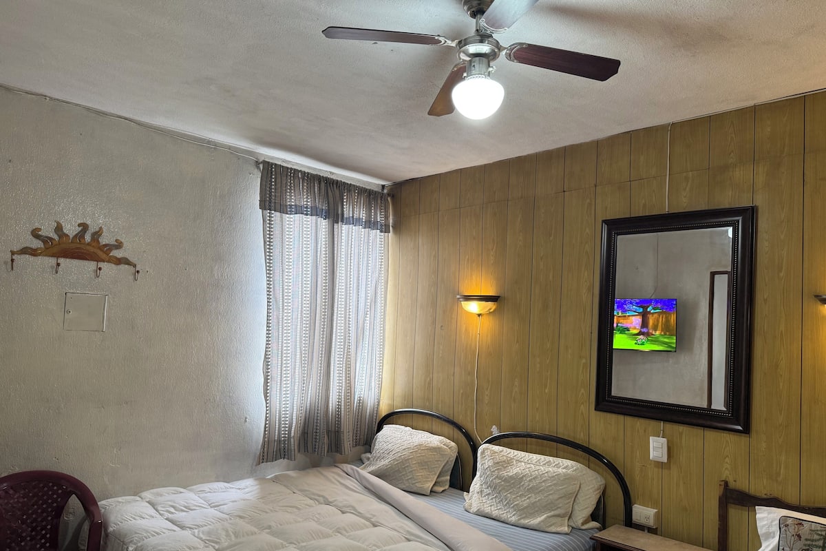 Een slaapkamer met een bed, een plafondventilator, een aan de muur bevestigde televisie en een wandpaneel van hout.