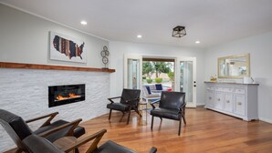 A modern living room with a fireplace, leather chairs, a dining area, and a view through a glass door. - Centrally located estate in Scottsdale with a heated pool, game room, and more! (Scottsdale)
