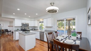 A modern kitchen with white cabinets, a central island, and a dining area with a table set for four. - Centrally located estate in Scottsdale with a heated pool, game room, and more! (Scottsdale)